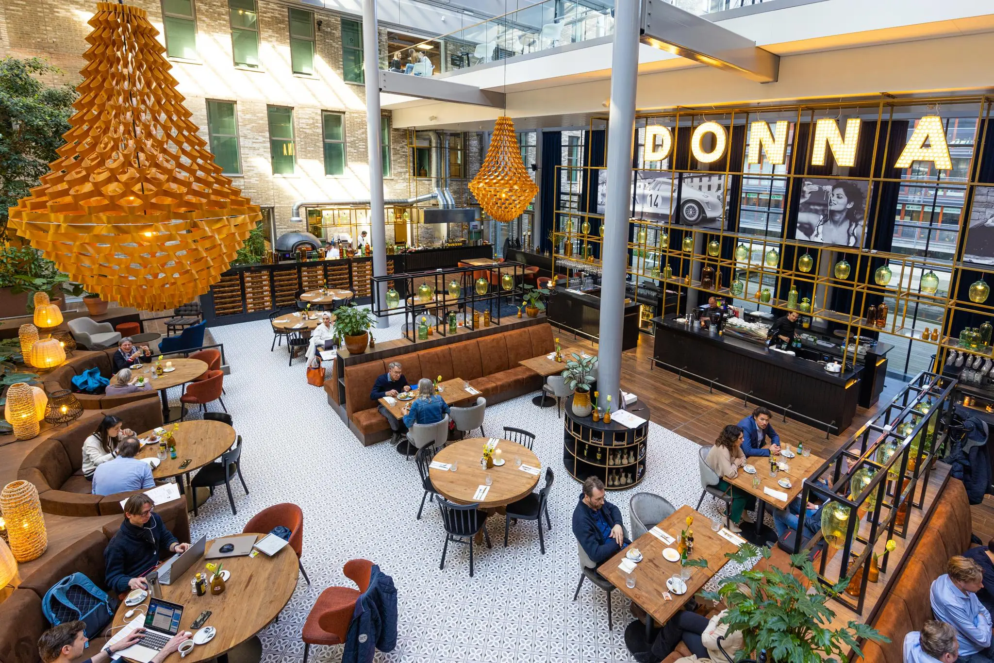 Modern en sfeervol restaurant genaamd DONNA aan de Prinses Beatrixlaan met hoge plafonds, grote hanglampen en mensen aan houten tafels.